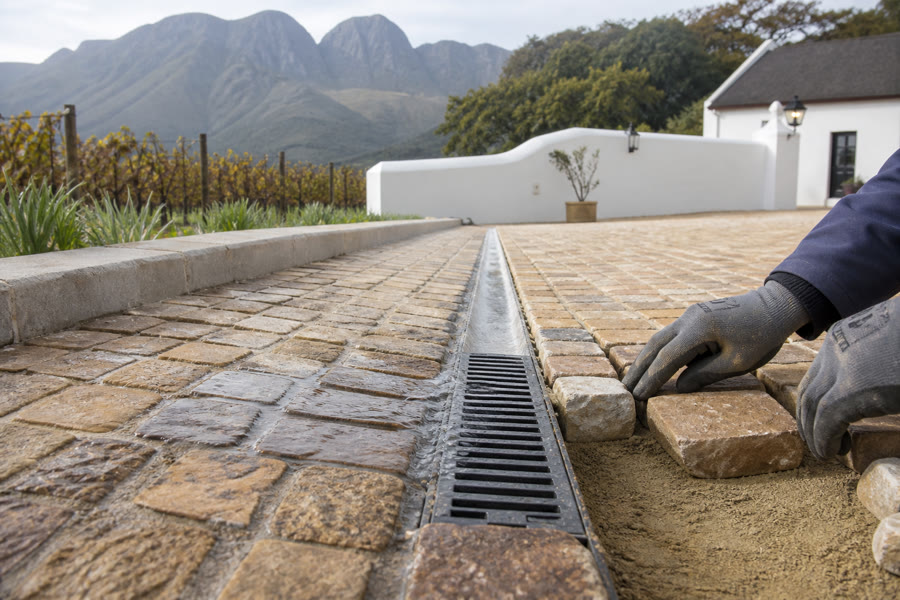 Sandstone cobbles being laid beside a slotted drainage channel at a Stellenbosch Cape Dutch property.