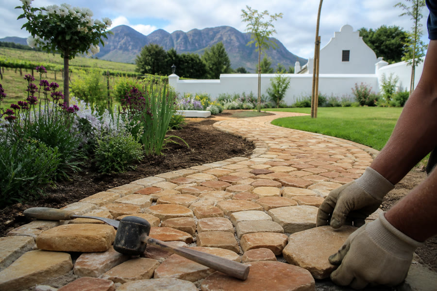 Winding sandstone cobble garden path being laid through flower beds at a Stellenbosch Cape Dutch home.